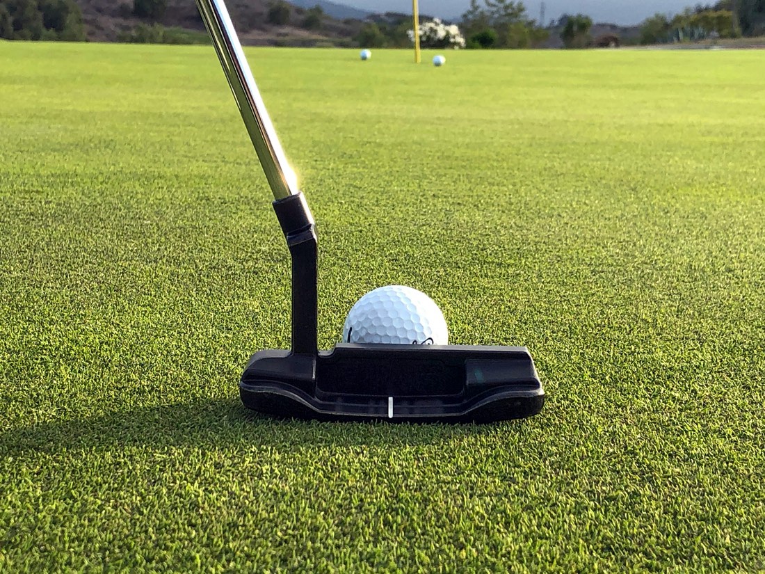 Putter lined up behind a golf ball on the green